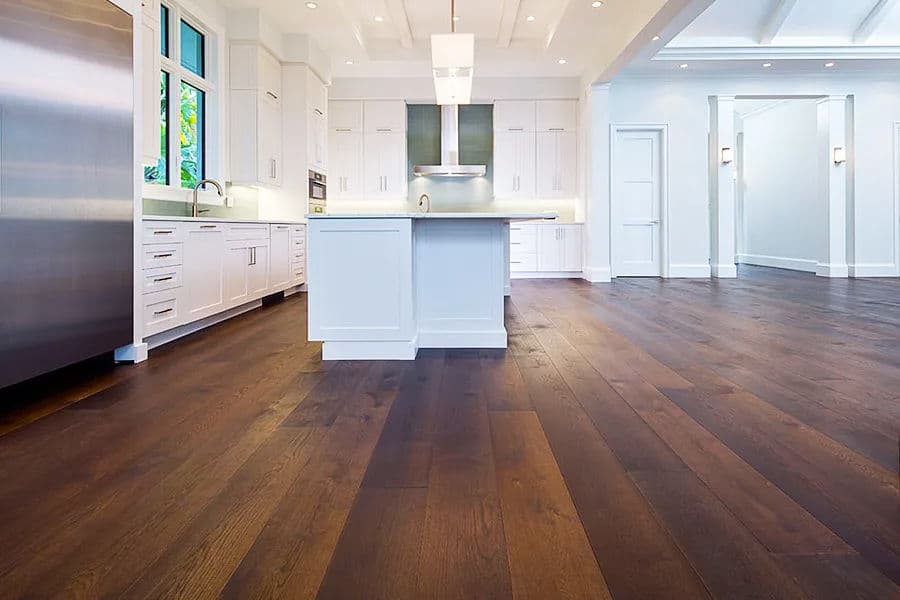 Modern kitchen with wood flooring, white cabinets, and stainless steel appliances, bright lighting.