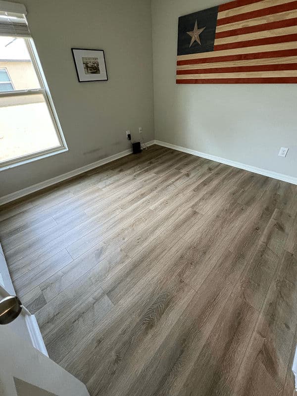 Empty room with wooden flooring and a large American flag on the wall. Bright natural light.