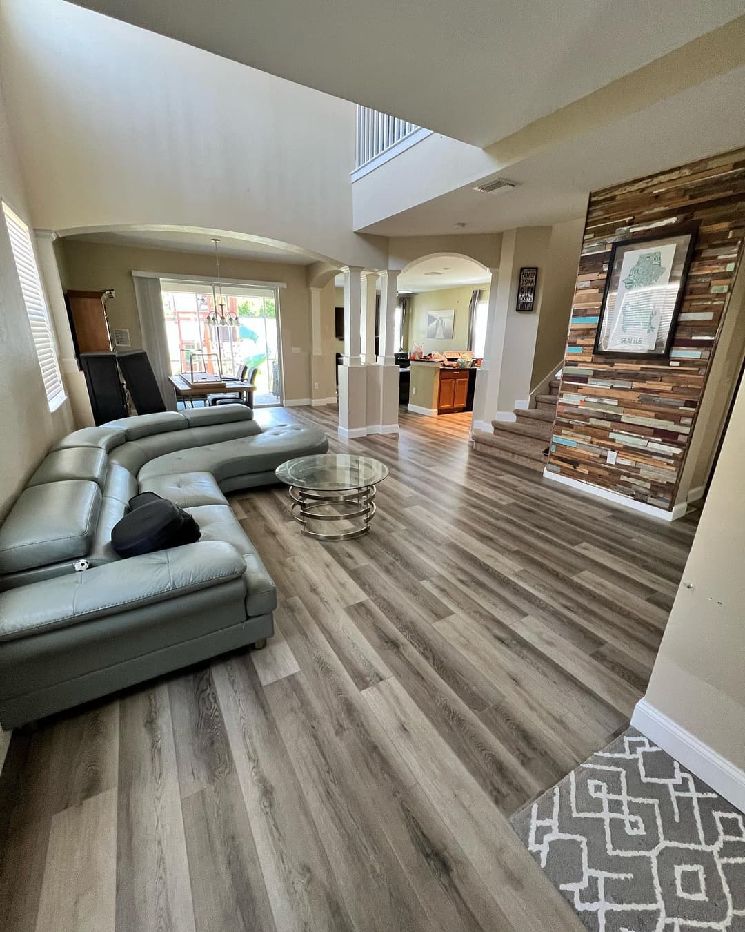 Modern living room with leather sectional, wood flooring, and open kitchen view. Bright and inviting.