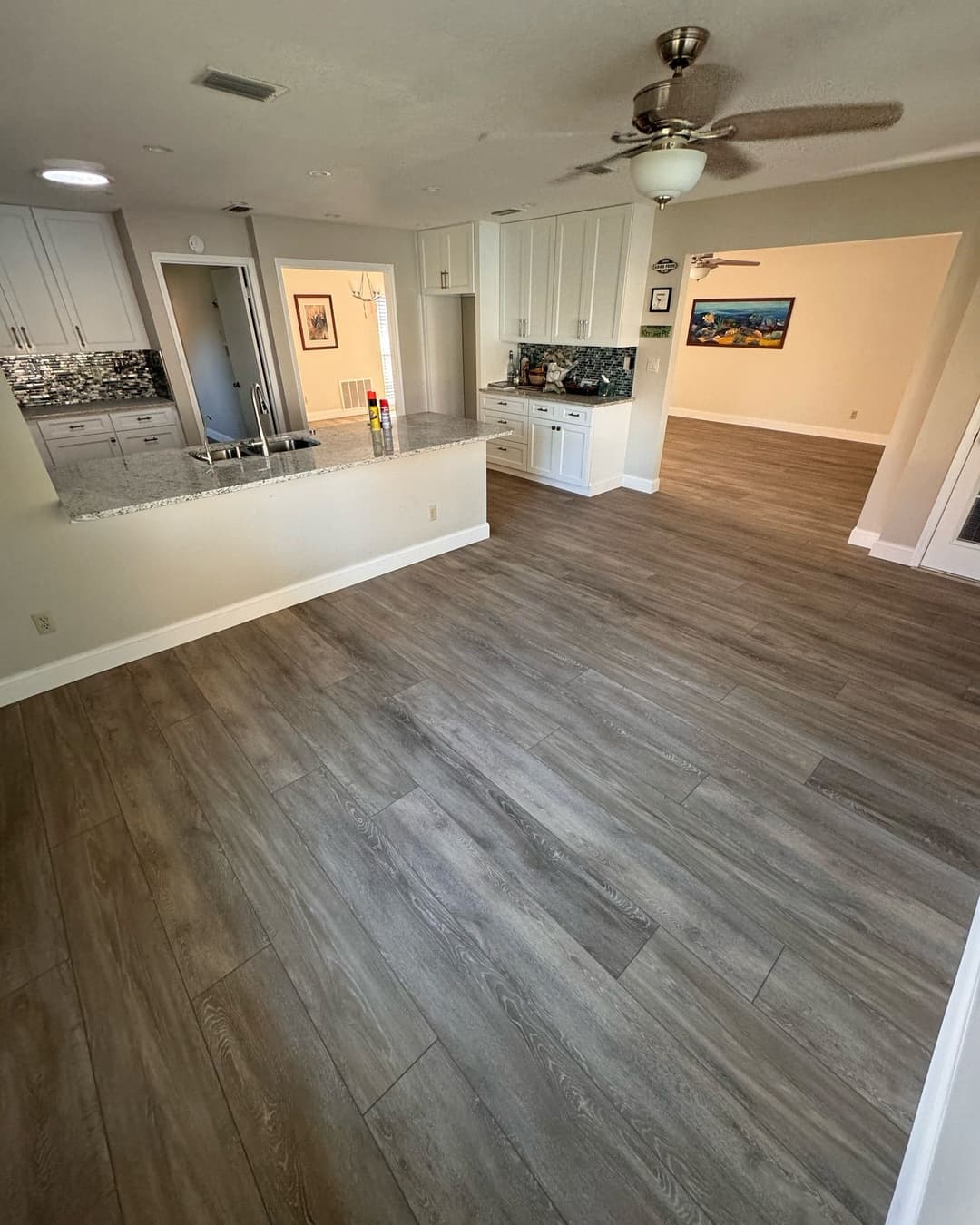 Spacious modern kitchen and living area with wood-like flooring and bright lighting.