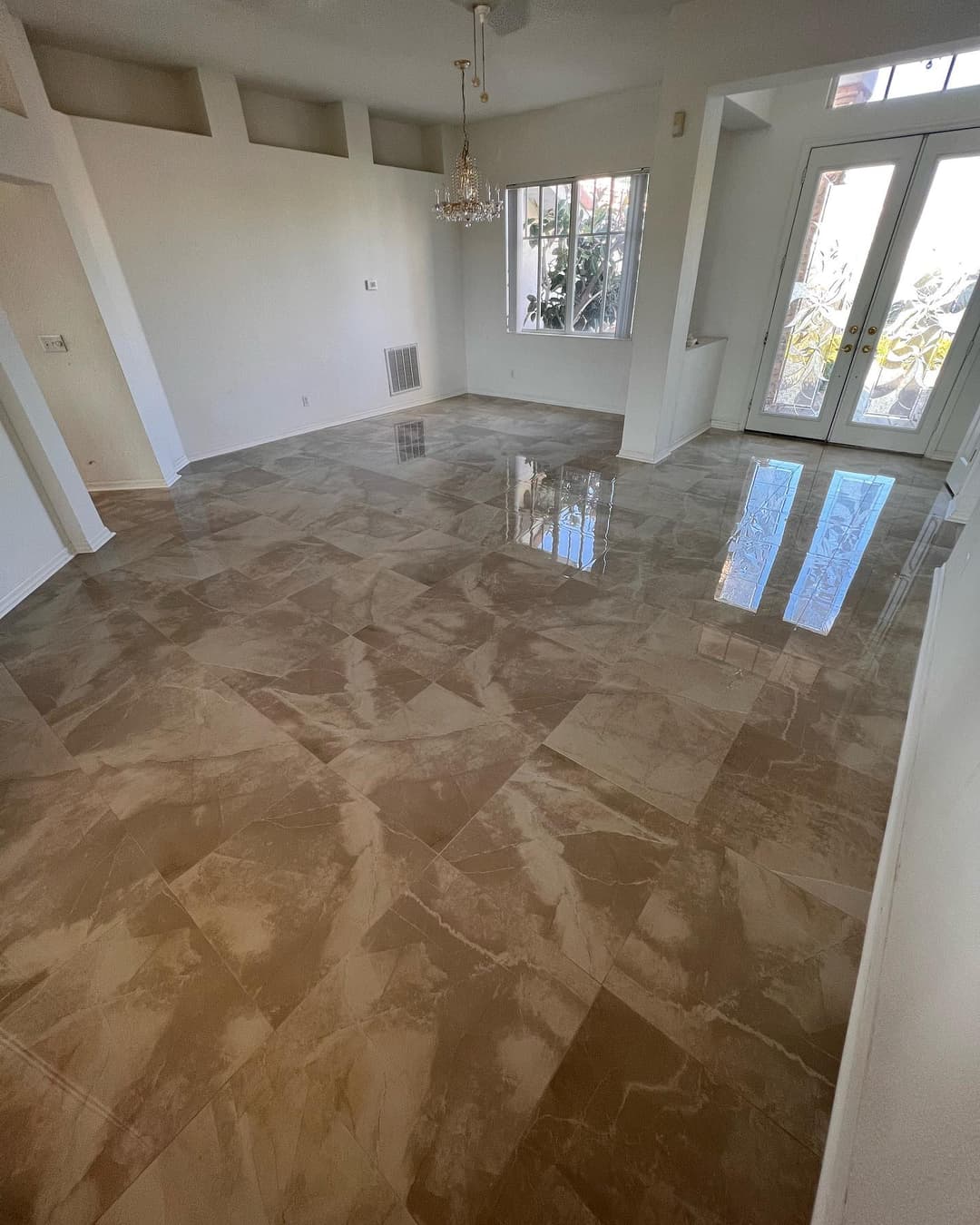 Spacious living room with polished marble floors, chandelier, and natural light.