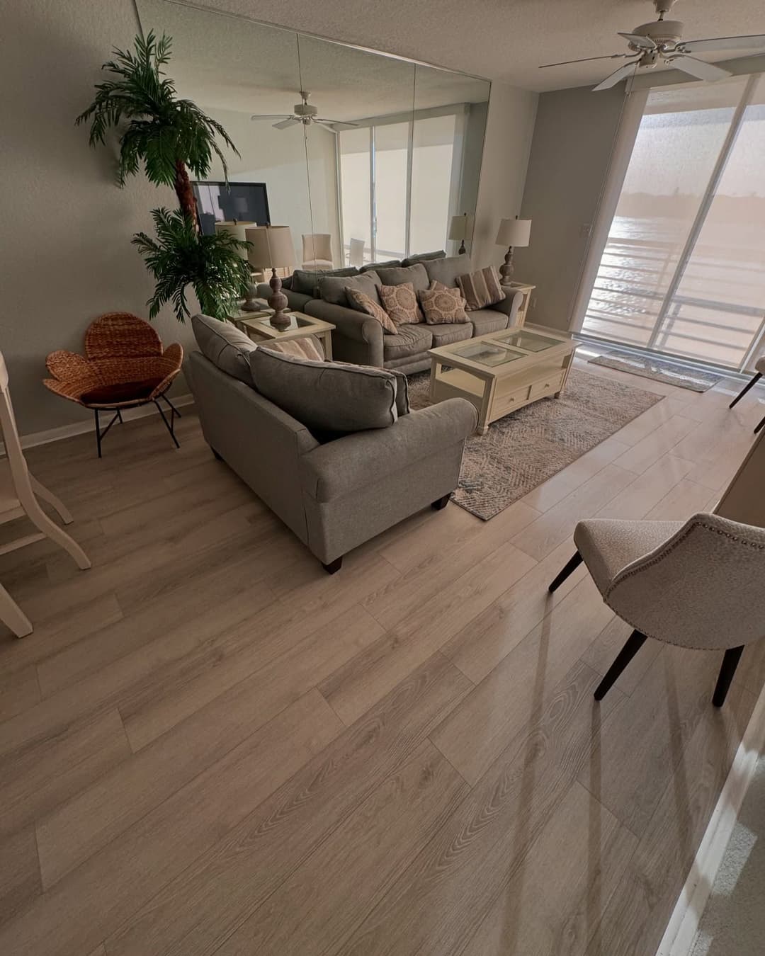 Cozy living room with gray sofa, woven chair, and large windows overlooking water view.