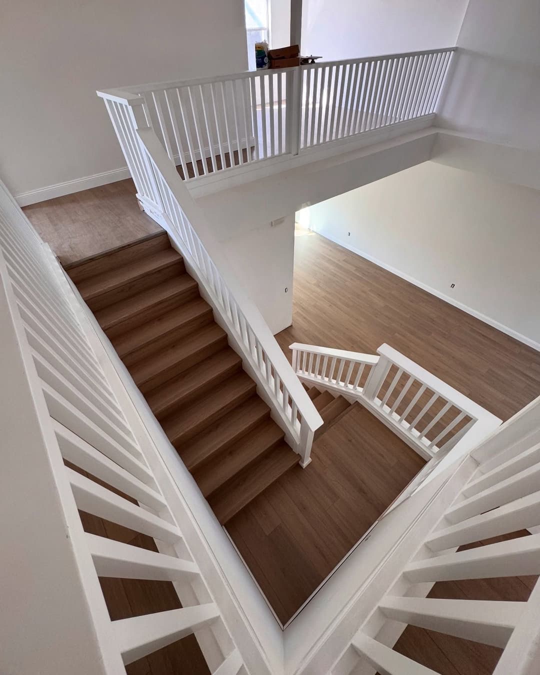 Modern interior with wooden stairs, white railings, and open space design. Bright natural light.